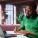 African american male teleworker writing personal notes at his desk in modern loft, remote job. Productive guy sitting at home office, using pen to take notes in his textbook. Camera B.